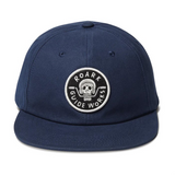 straight on view of a blue baseball cap woth a small circular patch in the center of the hat. The patch has a skull biting motorcycle handle bars with the word "roark" at the top of the circle and "guide Works" at the bottom.