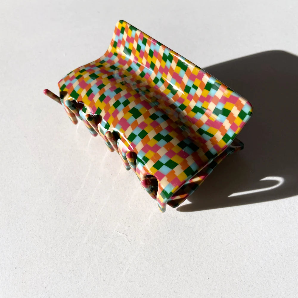 a checkered hair claw clip resting against a white background. The fun colors pop against the white background. 