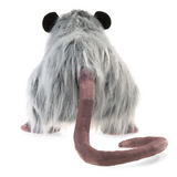 rear view of opossum puppet standing in front of white background. long mauve colored tail and dark black ears in contrast to background. 