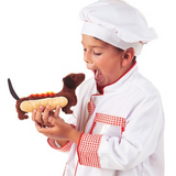 young child dressed in a chefs costume has an open mouth and is pretending to eat the hot dog hand puppet.