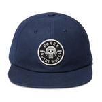 straight on view of a blue baseball cap woth a small circular patch in the center of the hat. The patch has a skull biting motorcycle handle bars with the word "roark" at the top of the circle and "guide Works" at the bottom. 