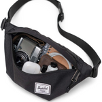 Black hip pack unzipped with a camera, notebook, wallet, headphones and lotions neatly tucked inside. 