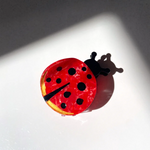LADY BUG CLAW CLIP SITTING ON A WHITE BACKGROUND. RED CIRCLE WITH10 BLACK DOTS OF VARIOUS SIZES WITH A SMALL BLACK PIE SHAPE CUT OUT TO DEFINE THE LADYBUGS WINGS. 