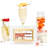 The same small white box is on display in front of a white background. Surronding the box are three artisanal cocktails. 