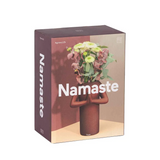 Tall box with brown sides that read "Namaste". Front of the box shows the vase holding flowers, casting a shadow on the wall behind it. 