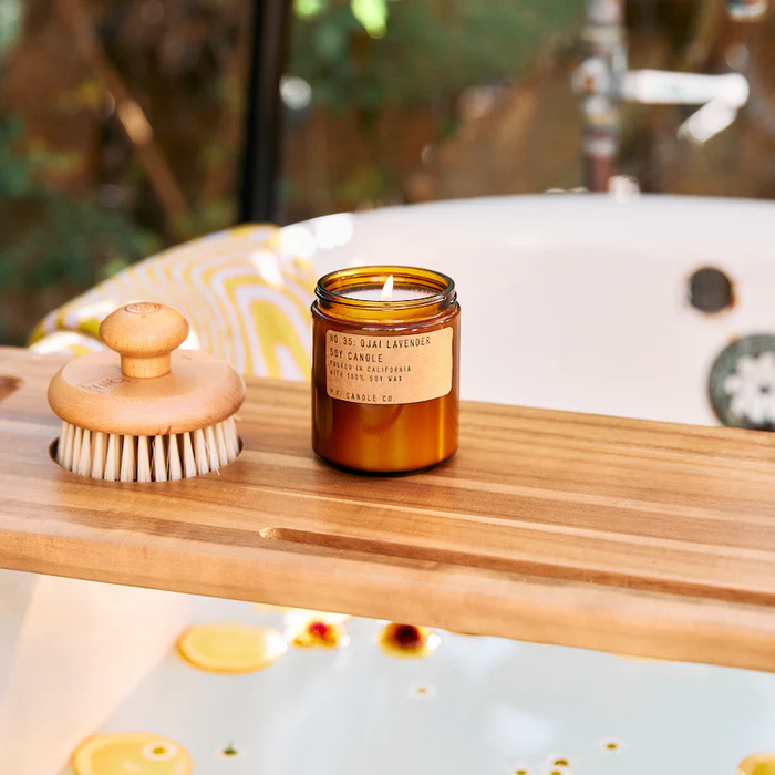 7.2oz Candle on a wood plank that's resting on a bathtub filled with water and sprinkled with florals. 