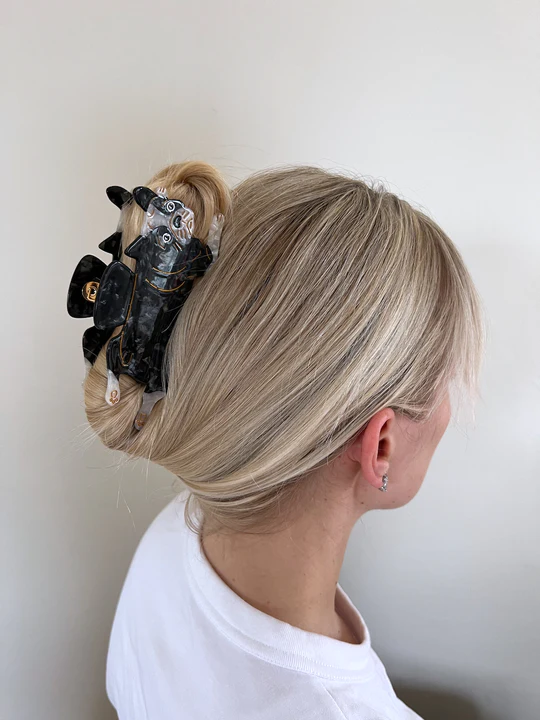 BLACK AND WHITE BULL DOG CLIP BEING USED TO TIE UP SOMEONES HAIR. 