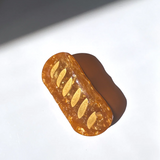 A AMBER BROWN HAIR CLIP WITH LIGHT BROWN MARKS  MADE TO LOOK LIKE A BAGUETTE SITS ATOP A WHITE SURFACE. 