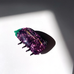 A MARBELED PURPLE CLAW CLIP WITH A GREEN TOP MADE TO LOOK LIKE AND EGGPLANT. THE CLIP SITS ON A WHITE BACKGROUND WHICH SHOWS THE DEPTH OF COLOR. 