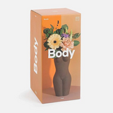 Body  vase box. Front graphic shows a body figure  from above the knees to the neck. There are flowers being displayed in the picture of the vase. The box is orange with  the word "body" displayed on the sides and across the main photo. 