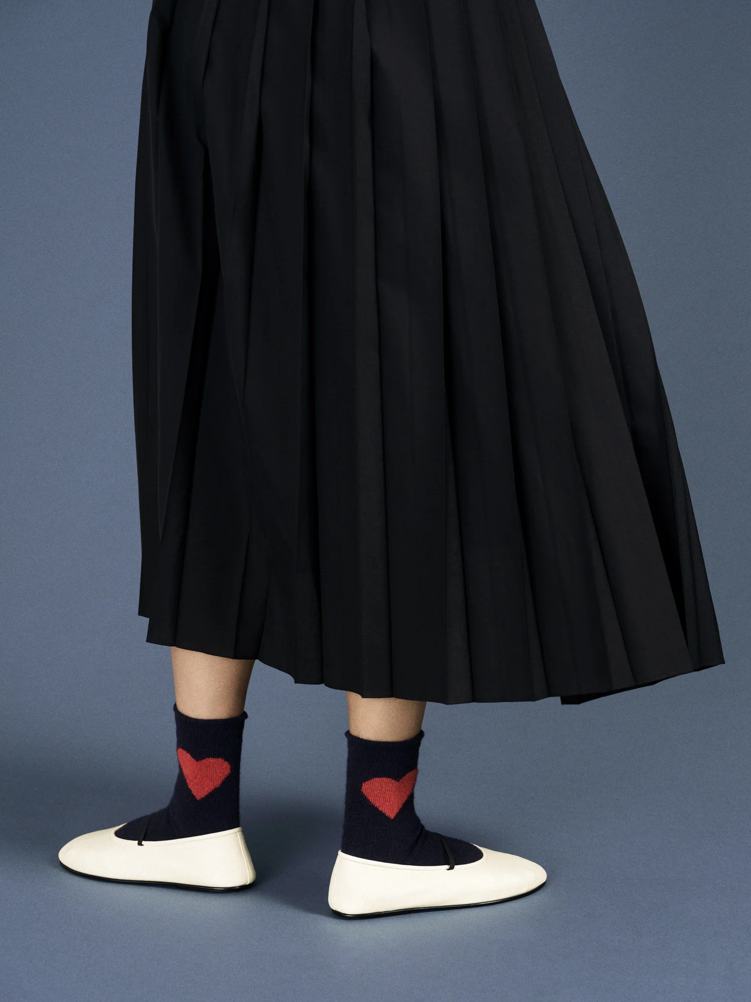 a person wearing a pleated skirt and the cashmere socks. The bright red heart pops against the blue base of the sock. 