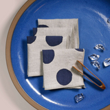 Set of 4 napkins neatly folded on a blue plate. The plate has wood tongs and a few pieces of ice scattered around. 