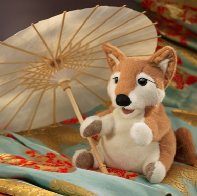 shiba inu puppy puppet relaxing on blankets  with an umbrella casting shade from the sun. 