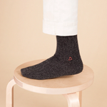 person standing in gray cashemere socks stands on a light wood stool. 