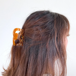A PERSON STANDS LOOKING AWAY FROM THE CAMERA WITH THEIR HAIR PULLED BACK USING THE PRETZEL CLIP. 