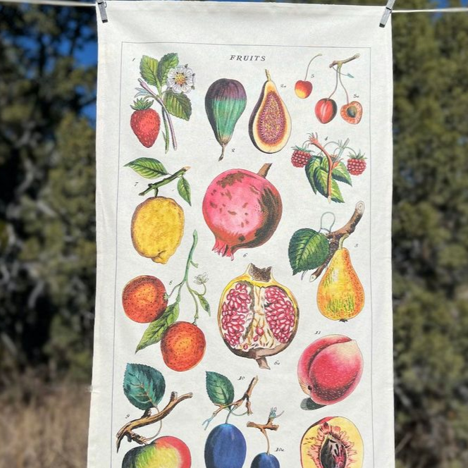 fruits tea towel hanging on clothes line with trees and a bright blue sky in the background.